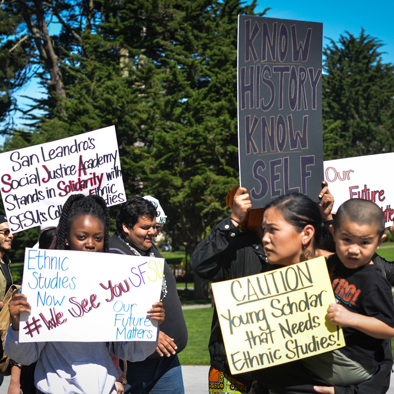 Several university students stand together with signs that advocate for ethnic studies curriculum.
